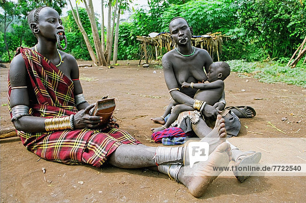 Mursi Tribal Woman With Pierced Lower Lip Serenading With Relative With Chongku