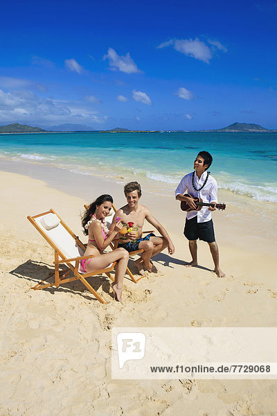 Hawaii  A Man Plays Ukulele For A Young Couple On The Beach.