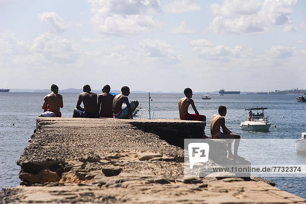 Young men sitting on concrete pier  Porto da Barra Beach  Salvador  Bahia State  Brazil