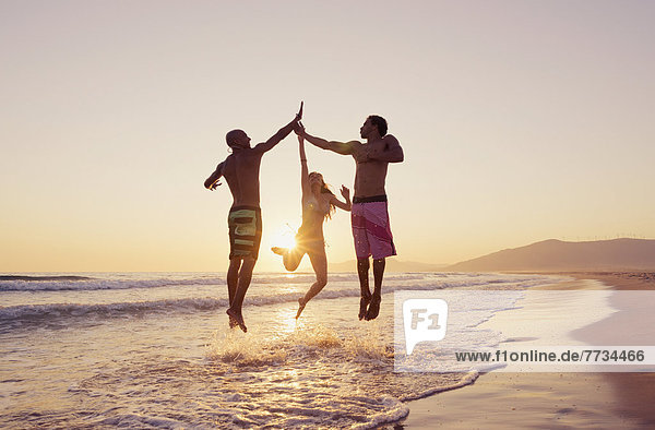 Three People Leaping In The Air To Clap Hands Together On A Beach At Sunset  Tarifa  Cadiz  Andalusia  Spain