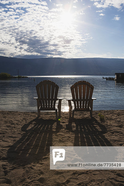 Two Beach Chairs On A Beach With The Sun Burst Out Of The Clouds And Long Shadows Of The Chairs On The Sand  Summerland British Columbia Canada