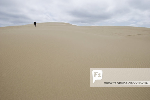 A Woman Walking Alone On A Sand Dune In The Distance  Florence Oregon United States Of America