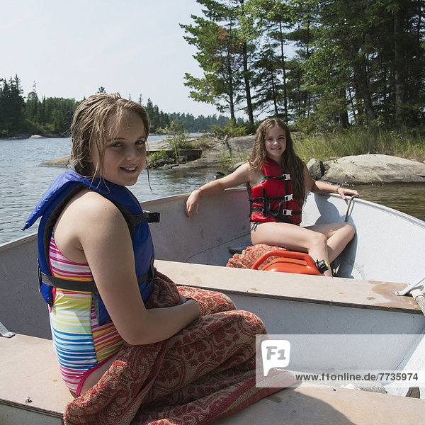 Tow Girls Sitting In A Boat By The Shore Of A Lake  Lake Of The Woods Ontario Canada