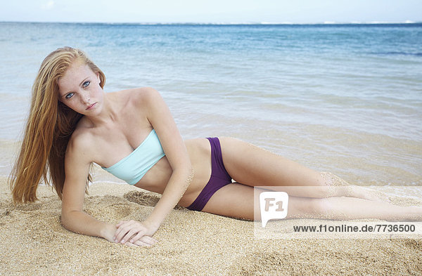 A young woman laying on the sand at the ocean's edge  kauai hawaii united states of america