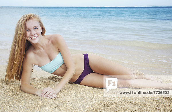 A young woman laying on the sand at the ocean's edge  kauai hawaii united states of america