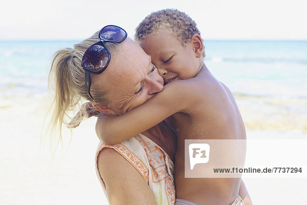 A mother and son in an embrace on the beach at the water's edge Hawaii united states of america