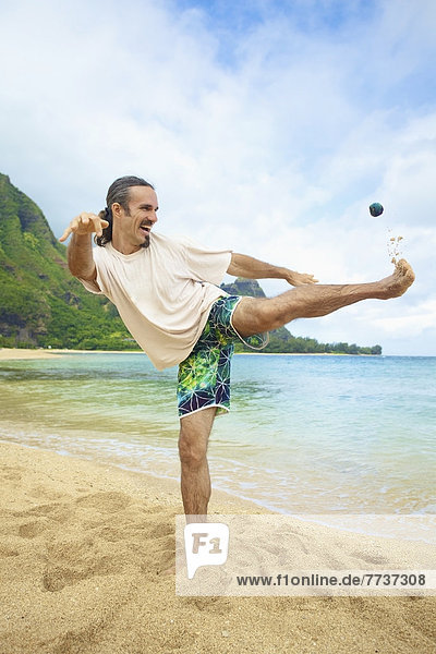 A man plays with his hackey sack in the sand at the water's edge Hawaii united states of america