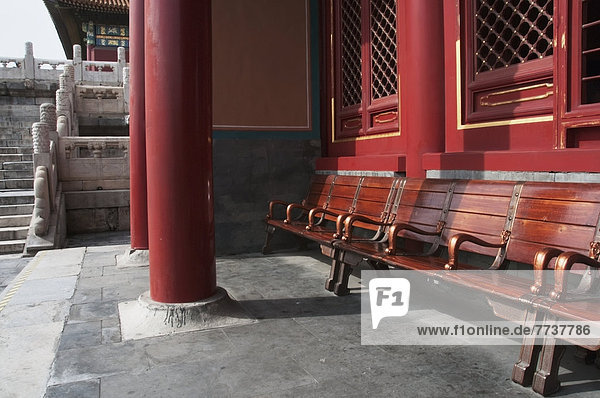 Wooden seating outside a building with a red wall and red pillars Forbidden city beijing china