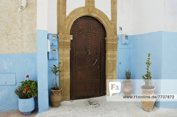 A house with an arched wooden door with rivets and painted blue walls in old town Rabat morocco