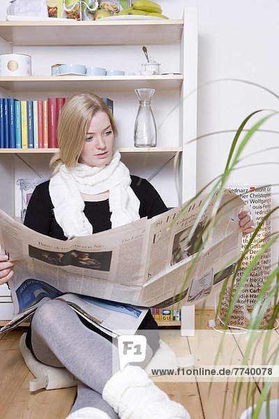 Blonde Woman is Sitting on the Floor Reading the Newspaper