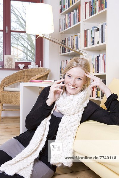 Frau sitzt telefonierend und lachend vor Sofa
