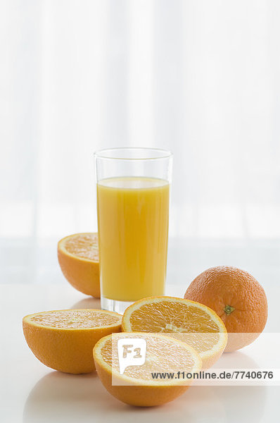 Glas Orangensaft mit Orangen auf Tisch vor weißem Hintergrund  Nahaufnahme