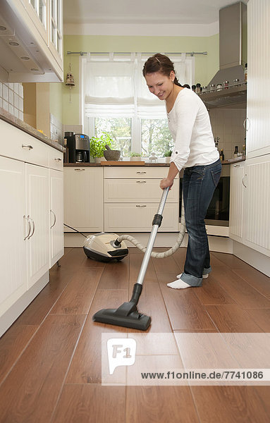 Junge Frau putzt Boden mit Staubsauger