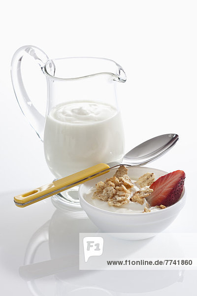 Schale Müslijoghurt mit Erdbeeren neben Joghurtkaraffe auf weißem Grund  Nahaufnahme