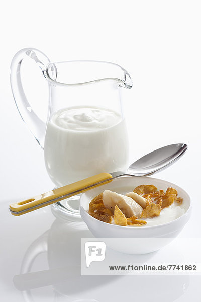 Schale Müslijoghurt mit Banane neben Joghurtkaraffe auf weißem Grund  Nahaufnahme
