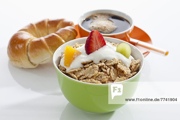 Schale mit Müsli  Joghurt und Früchten mit Kaffeetasse und Croissant auf weißem Hintergrund