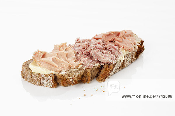 Scheibe Bauernbrot mit Butter und Wurst auf weißem Grund Nahaufnahme