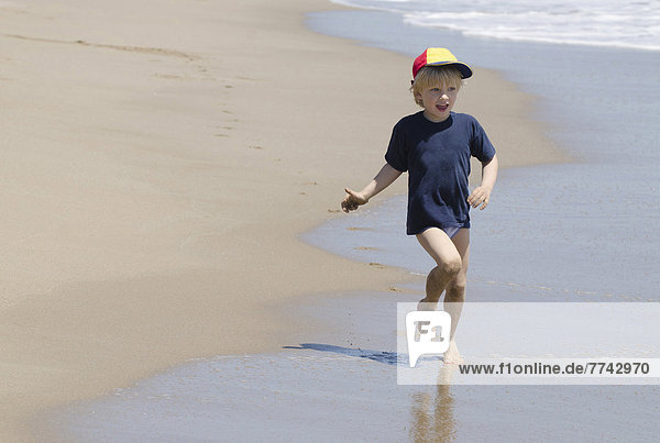 Spanien  Junge mit Schirmmütze läuft am Strand