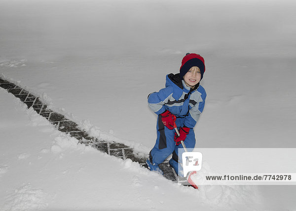 Österreich  Junge beim Schneeräumen mit Schneeschaufel