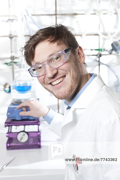 Deutschland  Porträt eines jungen Wissenschaftlers  der chemische Prozesse vorbereitet  lächelnd