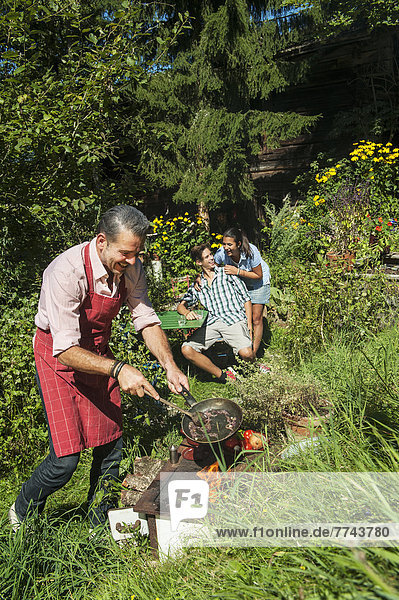 Österreich  Salzburger Land  Mann kocht für seine Familie im Garten