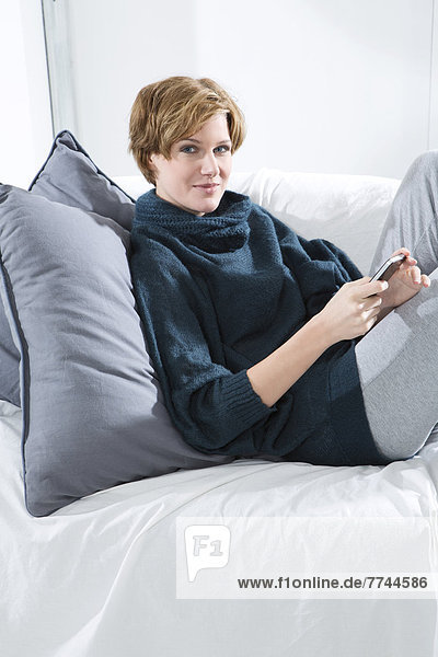 Junge Frau mit Handy auf der Couch  Portrait