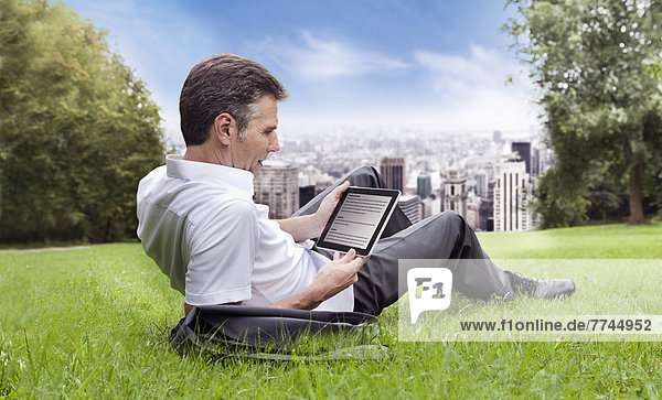 USA  New York  Man sitting on grass and using digital tablet  city in background