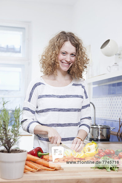 Young woman chopping vegetables in kitchen  smiling  portrait