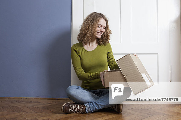 Young woman sitting on floor and opening postal package  smiling
