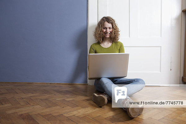 Young woman sitting on floor and using laptop  smiling  portrait