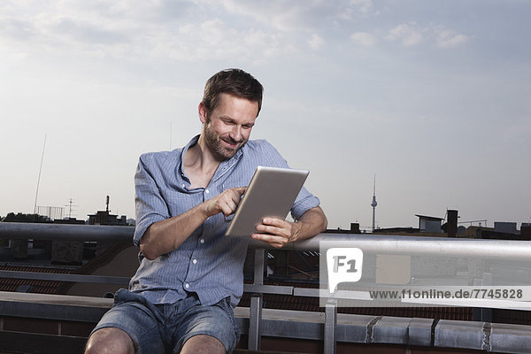 Man using digital tablet on roof terrace  smiling