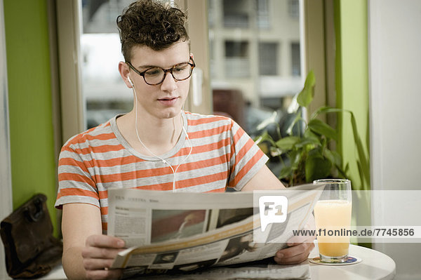 Junger Mann liest Zeitung im Café