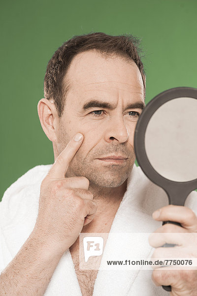 Mann im Bademantel schaut in einen Kosmetikspiegel