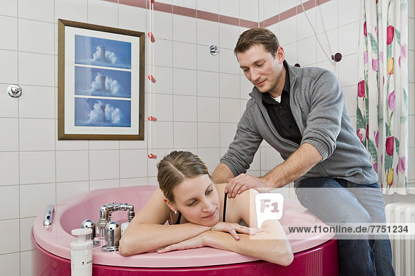 Der werdende Vater massiert seiner Frau während der Entbindung in der Entbindungswanne die Schultern