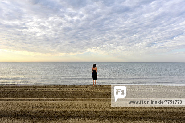 Woman wearing a black dress standing by the sea  moody clouds