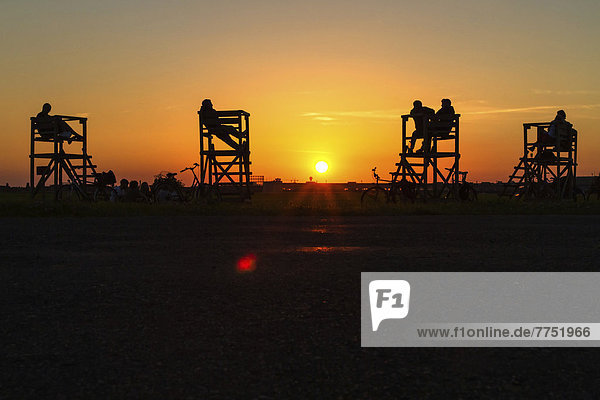 People sitting on raised seats on Tempelhof Airfield in the evening sun