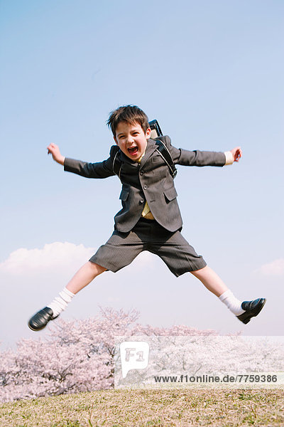 Young boy in school uniform jumping on grassland