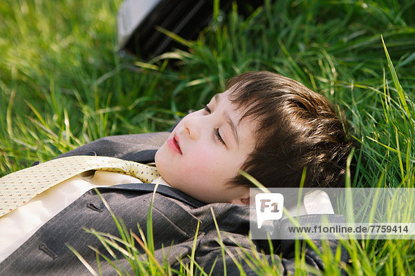 Young boy in school uniform laying on grassland