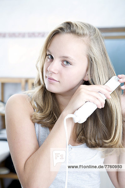 Teenage girl using hair straightener