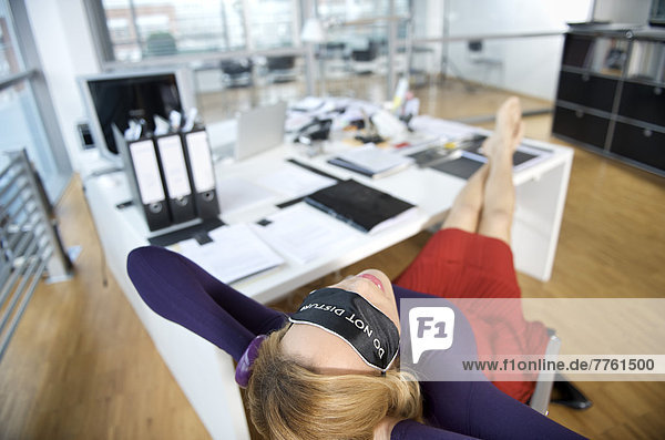 Frau mit Schlafmaske  entspannt im Büro