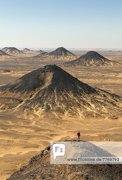 Ein Wanderer erklimmt die Spitze eines vulkanischen Pyramidebergs in der Schwarzen Wüste