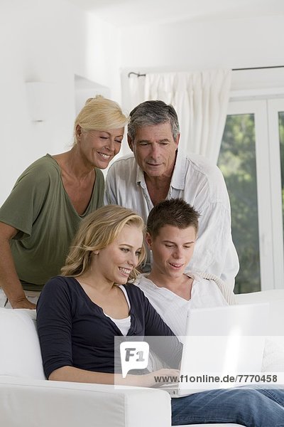 Mature couple and young couple at home  looking at laptop