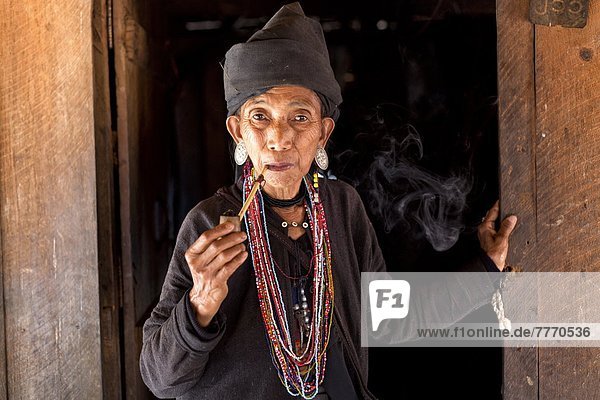rauchen rauchend raucht qualm qualmend qualmt nahe Frau Tradition Wohnhaus Eingang Hügel bunt schwarz Dorf Myanmar Asien Kleid Shan Staat Volksstamm Stamm