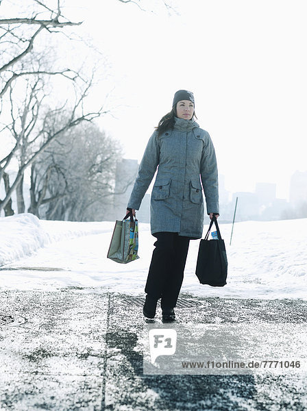 Junge Frau mit Einkaufstüten auf schneebedecktem Weg