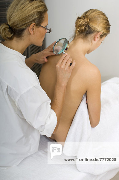 Female doctor examining beauty spots with magnifying glass on woman's back
