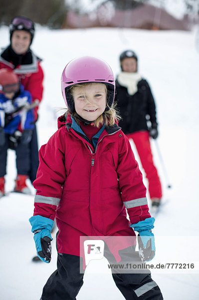 Porträt eines Mädchens in Skikleidung mit Familie im Hintergrund