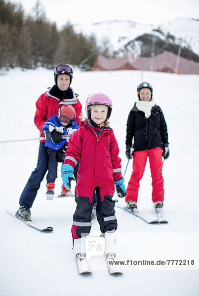 Portrait of happy little girl in ski-wear standing with family in background