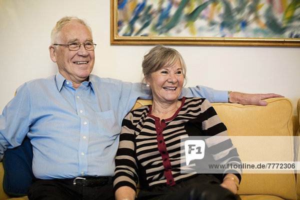 Glückliches Senior-Paar schaut weg  während es auf dem Sofa sitzt.