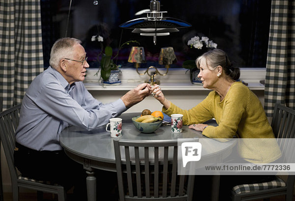 Seniorenpaar schaut sich an und hält die Hände über dem Esstisch.