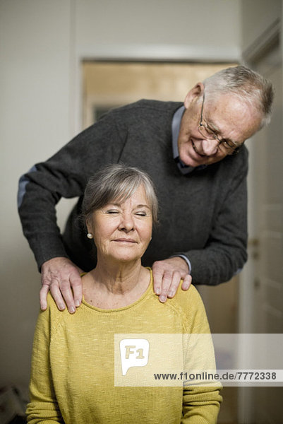 Älterer Mann  der der Frau zu Hause eine Schultermassage gibt